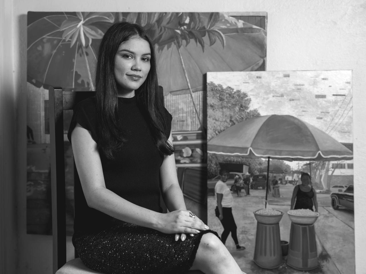 Ninfa Espinoza seated in her studio in front of two of her paintings